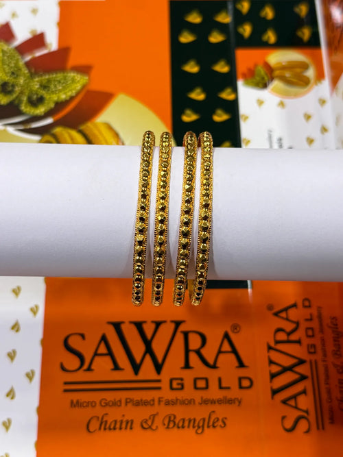 Three gold-plated chain bangles with bead detailing, displayed on a white cylindrical stand. The background features branded packaging for SAWRA GOLD.