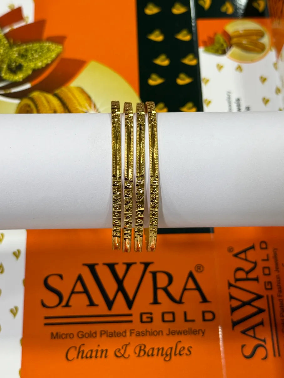 Four gold-plated chain and bangle bracelets displayed on a white cylindrical stand, with an orange SAWRA GOLD branded box visible underneath.